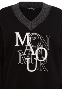 Schwarzer Pullover mit V-Ausschnitt und metallisch gefärbtem Kragen. Das Design umfasst weiße und silberne Texte in verschiedenen Schriftarten.