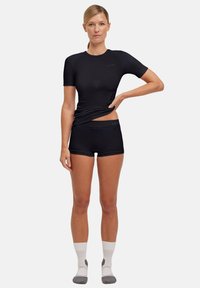 Chemise de sport noire à manches courtes avec une coupe ajustée, associée à un short noir. Le tissu semble lisse, avec un détail de marque subtil.