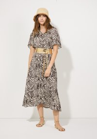 Robe à motif zèbre brun et crème avec des manches courtes, une ceinture métallique dorée et des sandales plates dorées ; modèle portant un chapeau en paille.