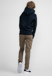 Marineblauwe hoodie met een trekkoord in de capuchon, gecombineerd met tan slim-fit broeken en witte sneakers met zwarte accenten. Eenvoudig ontwerp, zonder zichtbare patronen.