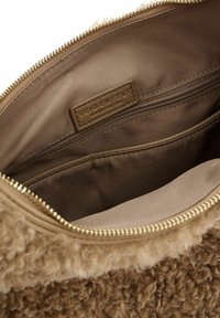 Intérieur de sac à main texturé marron avec une poche zippée et une étiquette en tissu. Extérieur doux et moelleux avec une doublure lisse. Détail de fermeture éclair en or.
