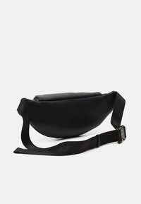 Sac en cuir noir avec une forme arrondie et une surface texturée. Il dispose d'une fermeture éclair plate et d'une bandoulière réglable avec une boucle.