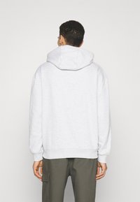 Sudadera gris claro hecha de tela suave, con capucha ajustable, puños acanalados y un corte relajado, combinada con pantalones cargo oscuros.