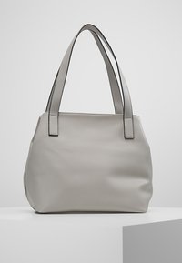 Sac fourre-tout en cuir gris avec deux poignées, une texture douce et une forme structurée légèrement arrondie. Présente des accents noirs contrastants sur les poignées.