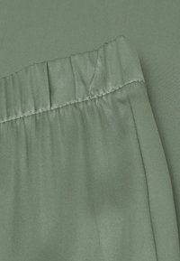 Groene satijnen stof met een gather-elastische tailleband, soepele textuur en subtiele glans, die een vloeiende en zachte uitstraling benadrukt.