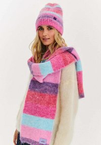 Różowy, niebieski i fioletowy zestaw czapki i szalika w paski. Szalik ma różne wzory pasków. Materiał wydaje się miękki i puszysty.