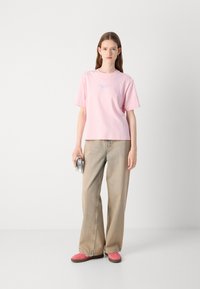T-shirt in cotone rosa a maniche corte, con un piccolo logo blu sul petto. Abbinato a jeans a gamba larga di colore chiaro e scarpe rosa.