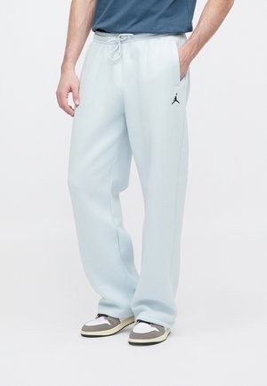Man draagt lichtblauwe joggingbroek met trekkoord in de taille en zwarte Jumpman-logo, gecombineerd met grijze en witte sneakers.