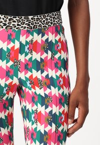 Bunte Leggings mit einem geometrischen Muster in Pink, Grün, Blau und Weiß, mit einem Leopardenmuster am Bund und glatter Textur.