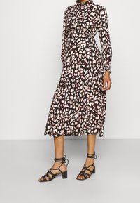 Långärmad, knapp-up klänning i svart med rosa och vit leopardmönster. Uppsvingad kjol, knähög längd, kombinerad med svarta remsandaler med blockklack.