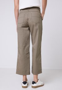 Pantaloni a gamba larga in khaki, realizzati in morbido cotone. Presentano due tasche posteriori e una vita semplice. Indossati con sneakers bianche.