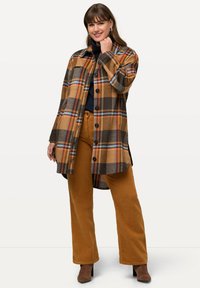 Brun rutigt skjortjacka med orange och blå accenter, med en knapp-på framsidan och sidslitsar. I kombination med bruna kordbyxor.