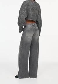 Szerokie dżinsy w szarym denimu z przetarciami. Posiadają pięć kieszeni i detale w postaci przeszyć. Połączone z krótkim, teksturowanym swetrem.