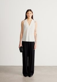 Άσπρο αμάνικο τοπ με V-λαιμόκοψη, συνδυασμένο με μαύρο παντελόνι φαρδιάς γραμμής. Ύφασμα ομαλό, εφαρμοστό, και μια μικρή μαύρη τσάντα χειρός.