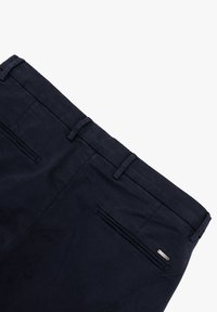 Pantaloni di cotone blu navy con una texture liscia, passanti per cintura e tasche posteriori con cerniere. Accento in metallo sulla tasca.