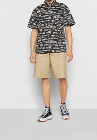 Chemise noire à manches courtes avec des motifs graphiques blancs, assortie à un short beige. Portée avec des baskets montantes noires avec des accents blancs.