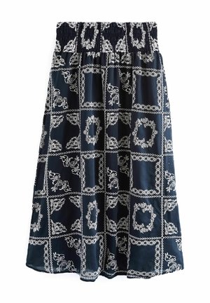 Femme portant une robe maxi noire sans manches avec des motifs floraux blancs et carrés, assortie à des sandales argentées à bout ouvert.