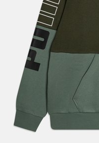 Sudadera verde oliva con un acabado texturizado, puños acanalados y un estampado negro en la manga. Detalle de bolsillo en la parte frontal.