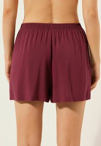 Pantalones cortos burdeos con cintura elástica, con un ajuste holgado y textura suave. Sin patrones visibles ni detalles de hardware.