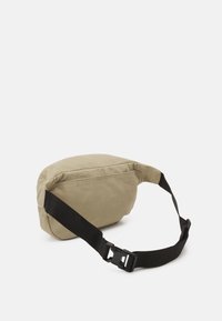 Khaki szövet keresztpántos táska, kerek formával, állítható fekete pánttal és műanyag csattal. Simább textúra, minimális design, oldalsó cipzáras záródás.