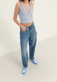 Svetle modrý tílko s krajkovým lemem, spárované s volnými modrými džíny a modro-bílými teniskami. Texturovaná tkanina kontrastuje s různými styly.