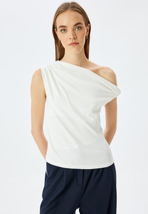 Top bianco monospalla realizzato in tessuto morbido, con dettagli drappeggiati e una vestibilità rilassata, abbinato a pantaloni blu navy.