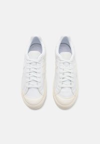 White sneakers featuring a smooth leather upper, traditional lace-up design, soft lining, and a rubber sole with a textured edge.