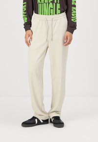 Lys beige strikkede bukser med elastisk midjebånd og snor, med en avslappet passform og ribbet tekstur, parret med svarte joggesko.