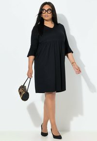 Černé šaty délky ke kolenům s výstřihem do V, tříčtvrtečními rukávy a nařaseným pasem. Doplněné černou kabelkou s leopardím vzorem a černými lodičkami.