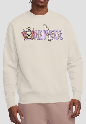 Person wearing a beige sweatshirt with "ONE PIECE" text and a skull with swords and pink wings graphic on the chest.