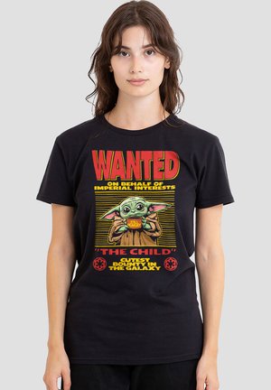 Woman wearing black T-shirt with red and yellow text "Wanted on behalf of Imperial interests" featuring Grogu holding a bowl labeled "Still Hungry."