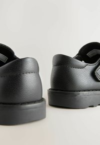 Schwarze Lederschuhe mit texturierten Oberflächen, abgerundetem Absatz und Gummisohle. Merkmale ein schlichtes Design mit minimalen Verzierungen.