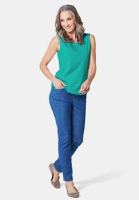 Groene mouwloze top gecombineerd met blauwe jeans en grijze ballerina's. De top heeft een ronde halslijn en een losse pasvorm, terwijl de jeans aansluitend zijn.