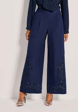 Marineblauwe broek met wijde pijpen en ingewikkelde kanten details aan de zoom, gemaakt van een soepel stof, met een getailleerde tailleband en plooien.
