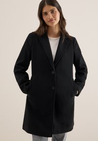 Manteau en laine noire mélangée avec un col cranté, deux poches avant et deux boutons. Le tissu a une texture douce et un design adapté.