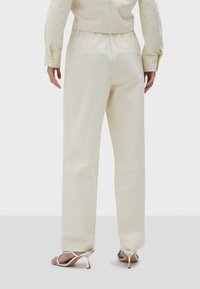 Crème-kleurige, wijde broek met een gladde textuur en een elastische tailleband. Voorzien van twee achterzakken en een relaxte pasvorm voor comfort.