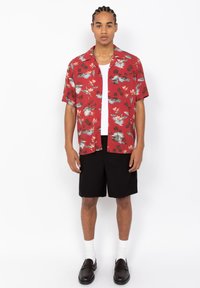 Rode korte mouwen shirt met tropisch bloemenpatroon, zwarte shorts, witte sokken en zwarte instappers. Ontwerpen omvatten palmen- en lotusmotieven.