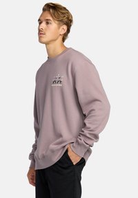 Light purple sweatshirt made of soft fabric features a ribbed neckline and cuffs, with a graphic print on the left chest area.