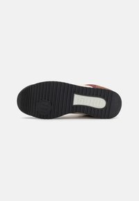 La suela del zapato presenta un caucho negro texturizado con ranuras verticales, un logo circular y una sección de marca en relieve en blanco.