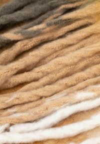 Włókna wełny w różnych odcieniach beżu, jasnobrązowego i szarości, o miękkim, teksturowanym wyglądzie i skręconych pasmach ułożonych w fale.