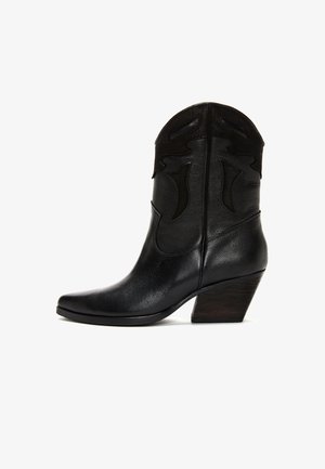 Bottes de cowboy en cuir noir avec un bout pointu, des coutures décoratives sur le dessus et un talon en bois effilé. Texture lisse sur l'ensemble.