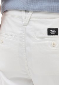 Witte katoenmix broek met een logo-label op de achterkant, twee achterzakken met knoopsluiting en zichtbare stikseldetails.