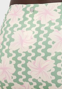 Blomstermønstrete skjørt i grønn, med store rosa blomster og bølgende hvite detaljer. Glatt stoff med en tettsittende linning og metallisk lukking.