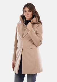 Cappotto beige in lana con taglio strutturato, chiusura frontale con bottoni e cappuccio imbottito removibile. Presenta tasche laterali e finitura testurizzata.