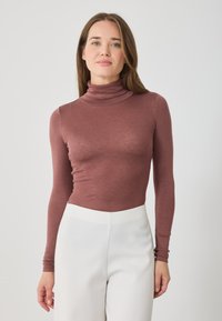 Cămașă cu mânecă lungă și guler închis, de culoare roz pal, fabricată dintr-un material moale cu o textură fină. Asortată cu pantaloni albi cu talie înaltă.