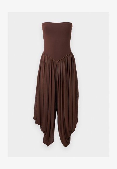 Καφέ ολόσωμη φόρμα χωρίς τιράντες με εφαρμοστό μπούστο και φαρδιά, draped και πλισαρισμένα παντελόνια που δημιουργούν μια αέρινη σιλουέτα.
