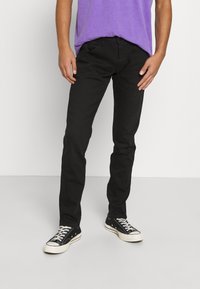 Svarta denimjeans med slim fit, med femficksdesign och bältesömmar, kombinerat med en lila t-shirt med rund hals och svarta sneakers.