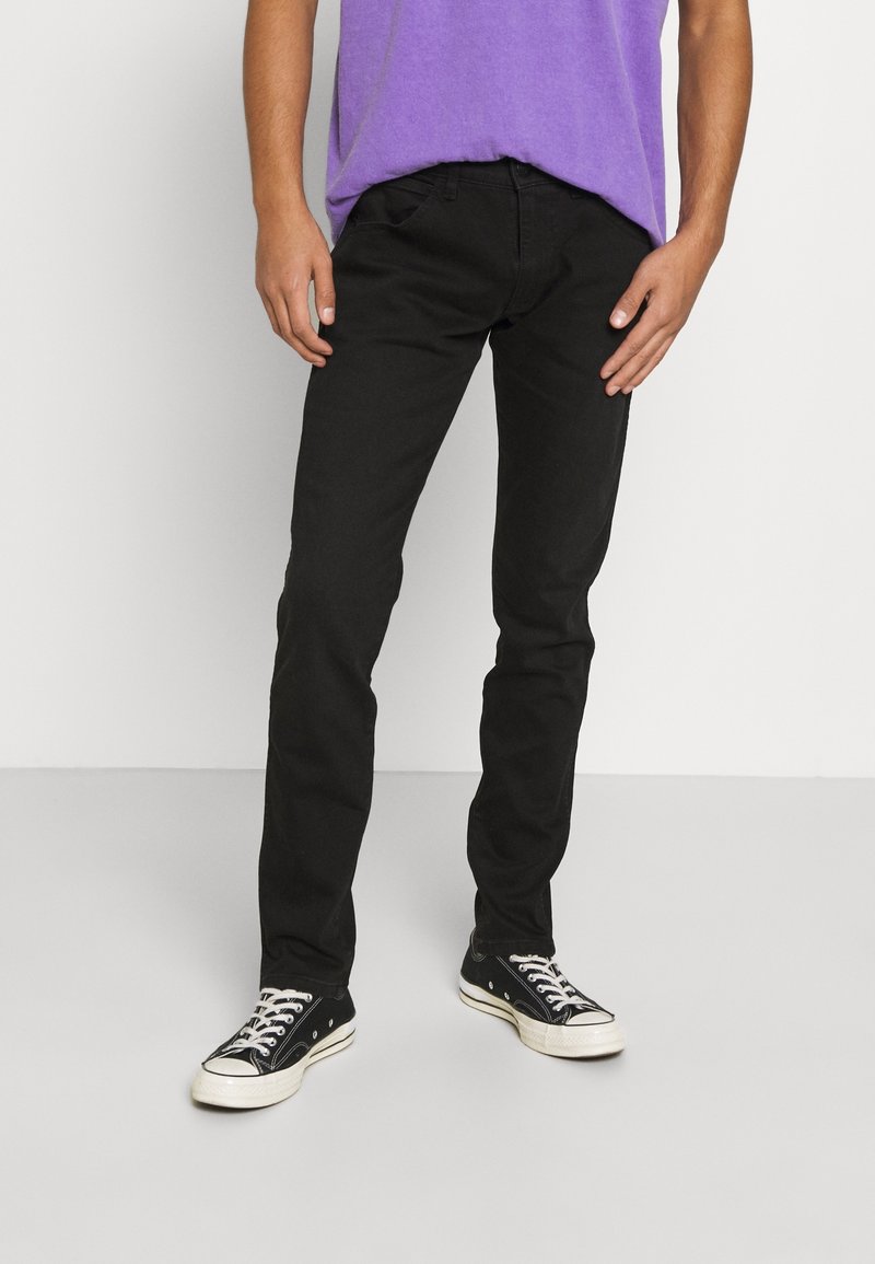 Svarta denimjeans med slim fit, med femficksdesign och bältesömmar, kombinerat med en lila t-shirt med rund hals och svarta sneakers.