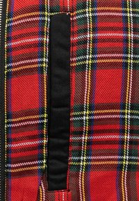 Tissu tartan rouge avec des accents noirs, présentant un motif plaid dense créé par des lignes entrecroisées en bleu, jaune et vert.