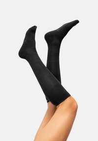 Calcetines negros hasta la rodilla, fabricados en un tejido suave con textura acanalada, que cuentan con puntera reforzada y detalles de soporte en el arco.